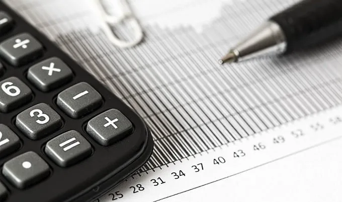 Um close-up de uma calculadora, uma caneta e um clipe de papel em um documento financeiro com números e um gráfico, simbolizando planejamento financeiro ou contabilidade - habilidades essenciais para qualquer pessoa que esteja explorando o que é freelancer on-line.